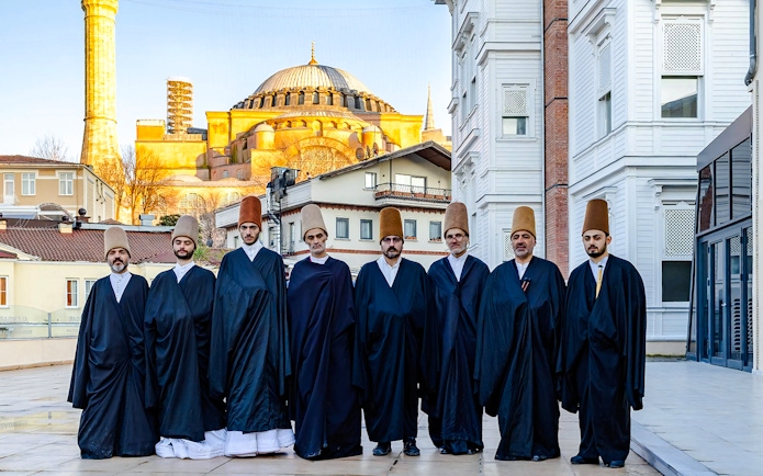 Whirling Dervishes in traditional attire with Hagia Sophia in Istanbul background.