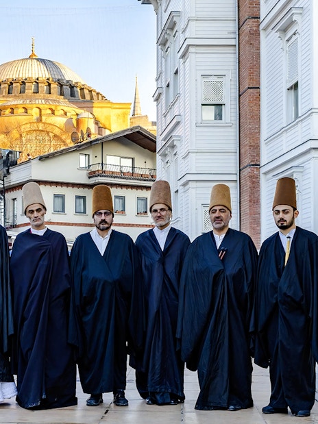 Whirling Dervishes in traditional attire with Hagia Sophia in Istanbul background.