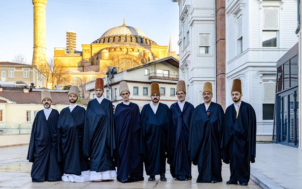 Whirling Dervishes in traditional attire with Hagia Sophia in Istanbul background.