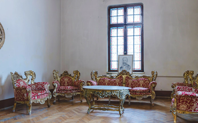 Lavish room with ornate red furniture and grand wall clock at Peles Castle.