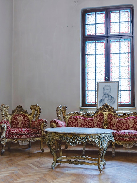 Lavish room with ornate red furniture and grand wall clock at Peles Castle.