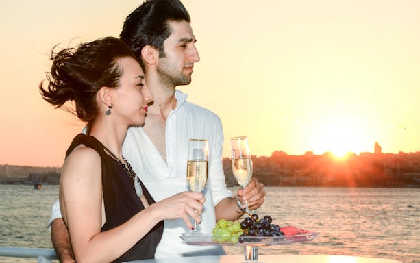 Couple enjoying champagne on a Bosphorus sunset cruise with city skyline in the background.