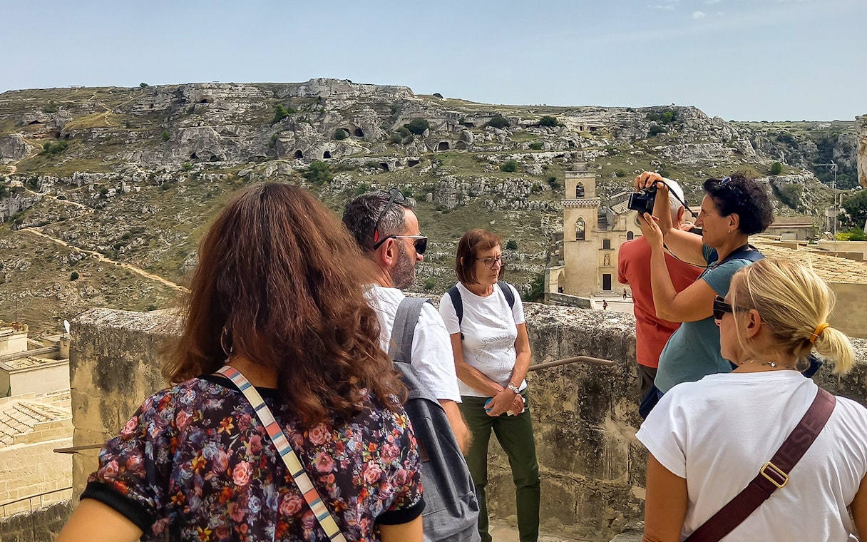 Tourists on a Matera bus tour with audio guide, overlooking ancient cave dwellings and Casa Grotta.
