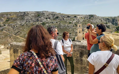 Tourists on a Matera bus tour with audio guide, overlooking ancient cave dwellings and Casa Grotta.