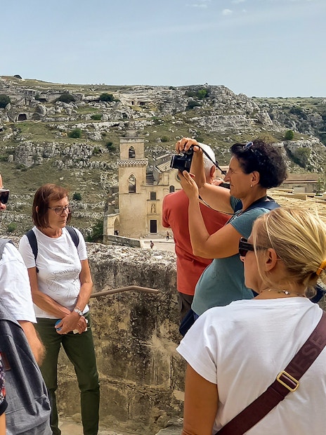 Tourists on a Matera bus tour with audio guide, overlooking ancient cave dwellings and Casa Grotta.