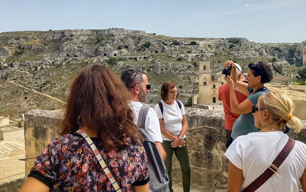 Tourists on a Matera bus tour with audio guide, overlooking ancient cave dwellings and Casa Grotta.
