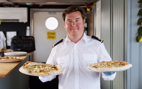 Crew member serving pizza on Stockholm cruise.