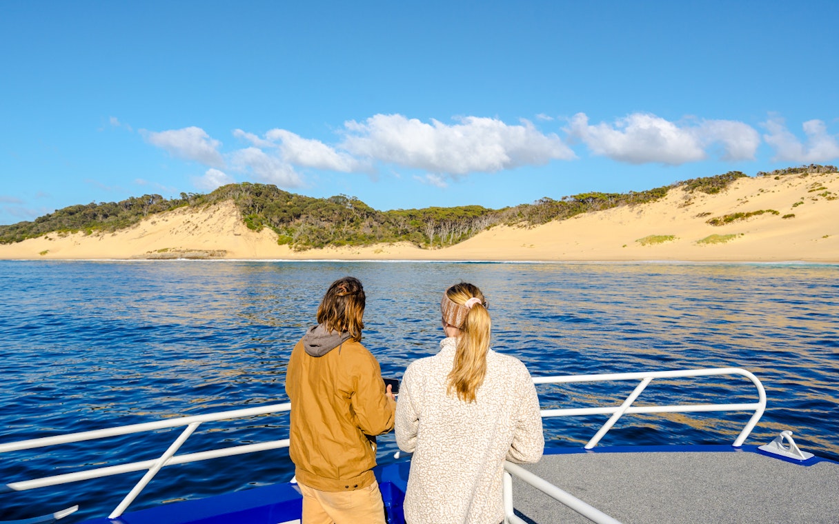 People on a boat viewing sandy dunes at Crescent Bay, Tasmania.