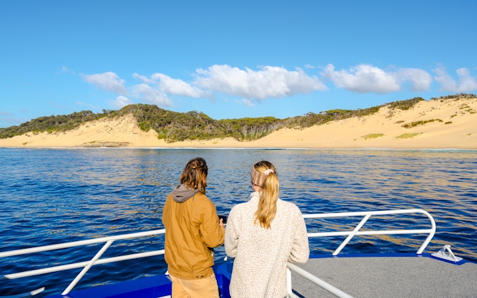 People on a boat viewing sandy dunes at Crescent Bay, Tasmania.