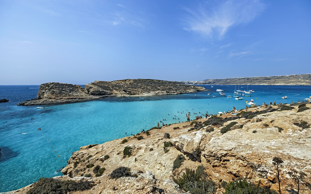 Blue Lagoon in Malta with clear turquoise water, rocky coastline, and anchored boats.