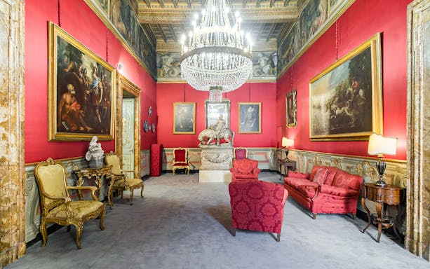 Art Patrizi Palace interior with red walls, ornate chandelier, classical paintings, and elegant furniture.
