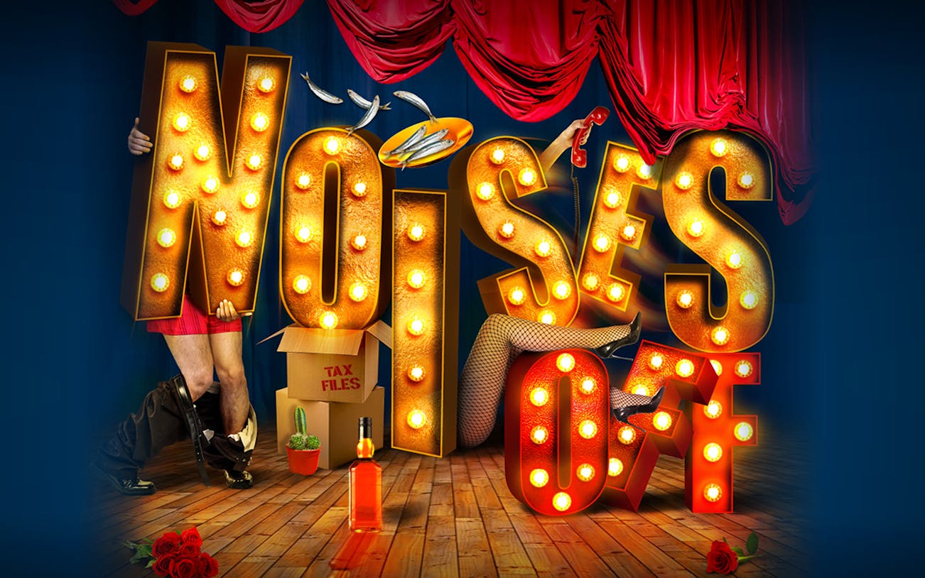 Theater stage with "Noises Off" in illuminated letters, props, and red curtains.
