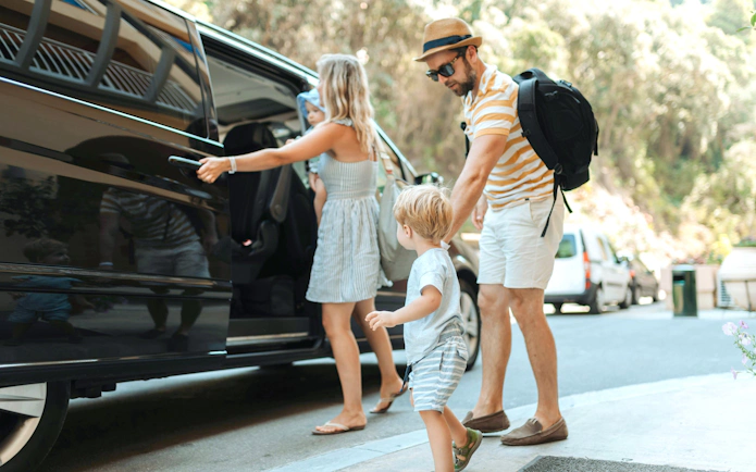 Parents with toddlers boarding a car for hotel pickup.