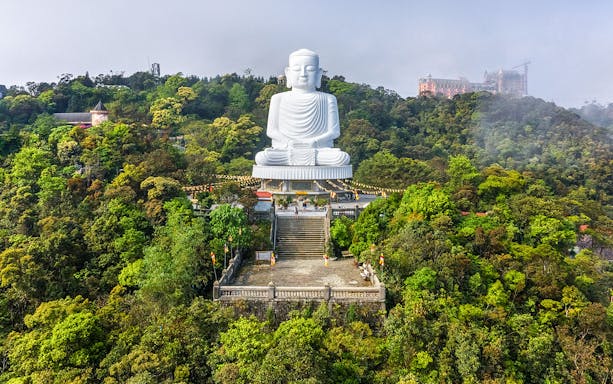 Aerial view of Linh Ung Pagoda with giant Buddha statue in lush forest, Vietnam.