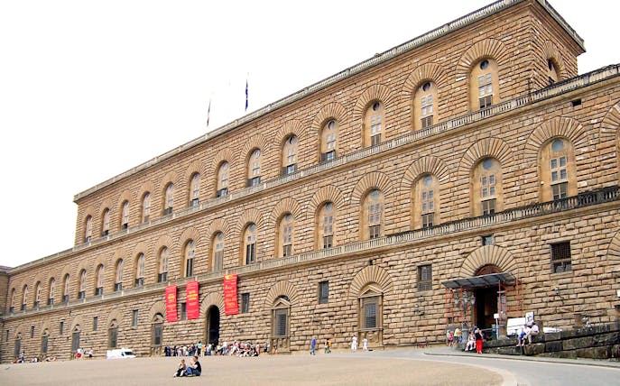 Pitti Palace facade in Florence, Italy, with visitors outside.