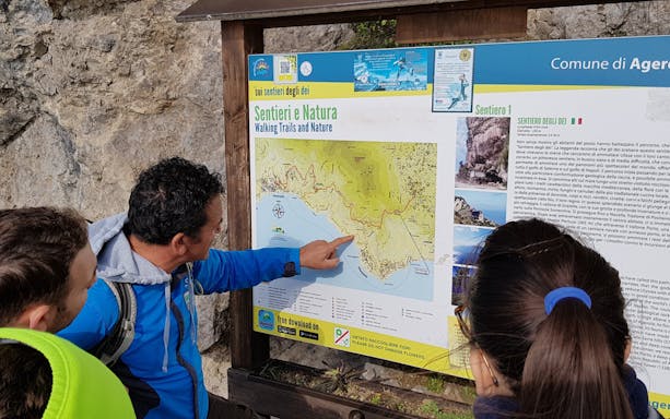 Tourist with guide examining information board for Path of the Gods trail, Italy.