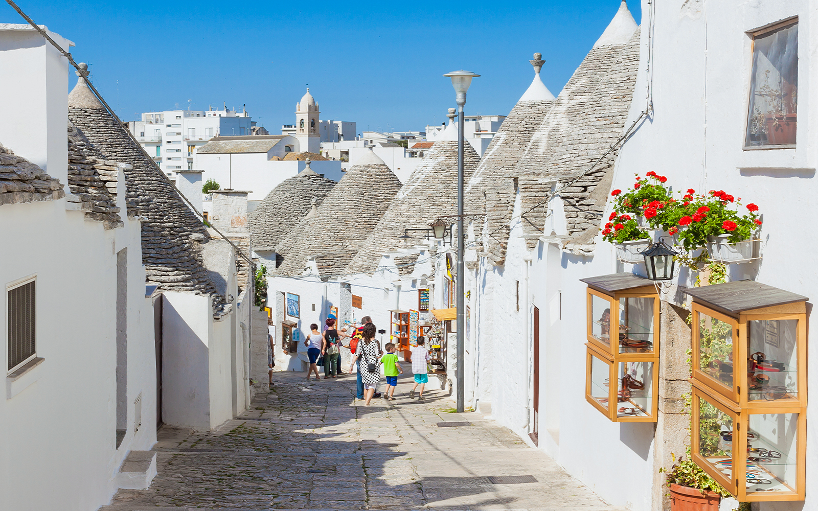 Trulli houses lining a cobblestone street in Alberobello, Apulia, with tourists exploring.
