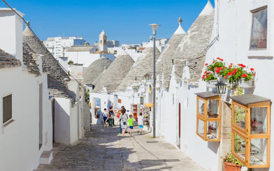 Trulli houses lining a cobblestone street in Alberobello, Apulia, with tourists exploring.