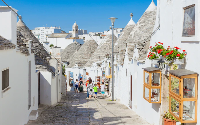 Trulli houses lining a cobblestone street in Alberobello, Apulia, with tourists exploring.