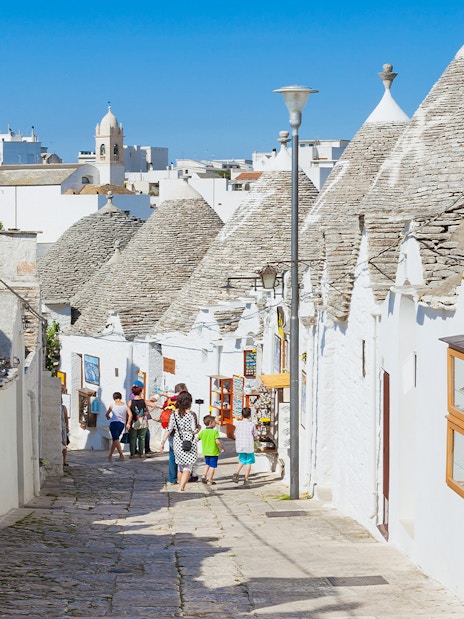 Trulli houses lining a cobblestone street in Alberobello, Apulia, with tourists exploring.