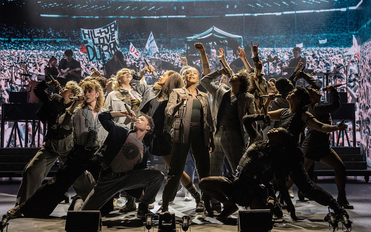 Performers on stage during "Just for One Day" show with a crowd backdrop.