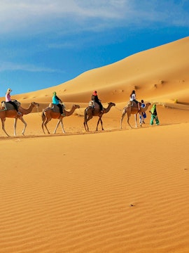 Tourists riding camels across Dubai desert dunes.