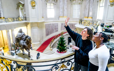 Visitors exploring a grand museum interior in Berlin with a statue and red carpet staircase.