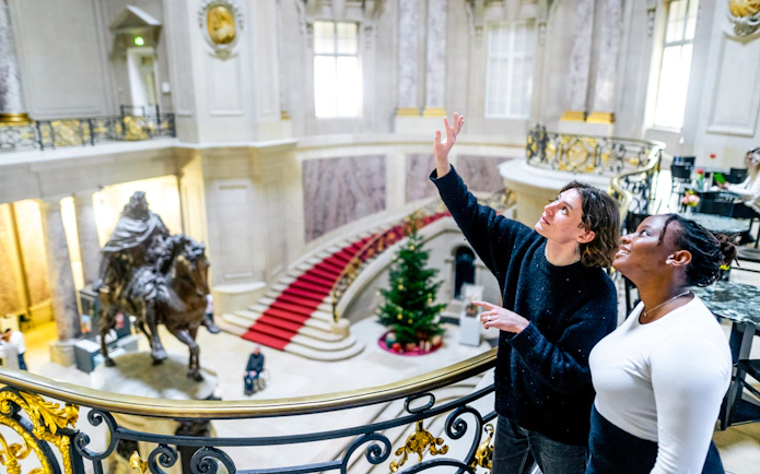 Visitors exploring a grand museum interior in Berlin with a statue and red carpet staircase.