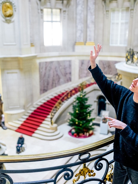 Visitors exploring a grand museum interior in Berlin with a statue and red carpet staircase.