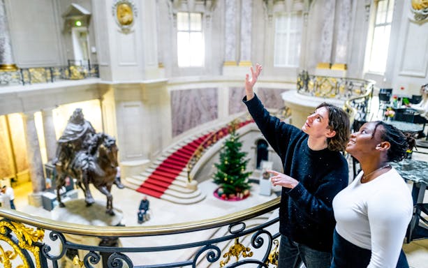 Visitors exploring a grand museum interior in Berlin with a statue and red carpet staircase.