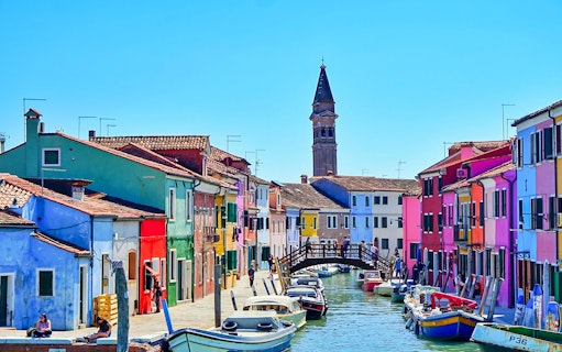 Colorful houses along a canal in Burano, Venice, with boats and a wooden bridge.