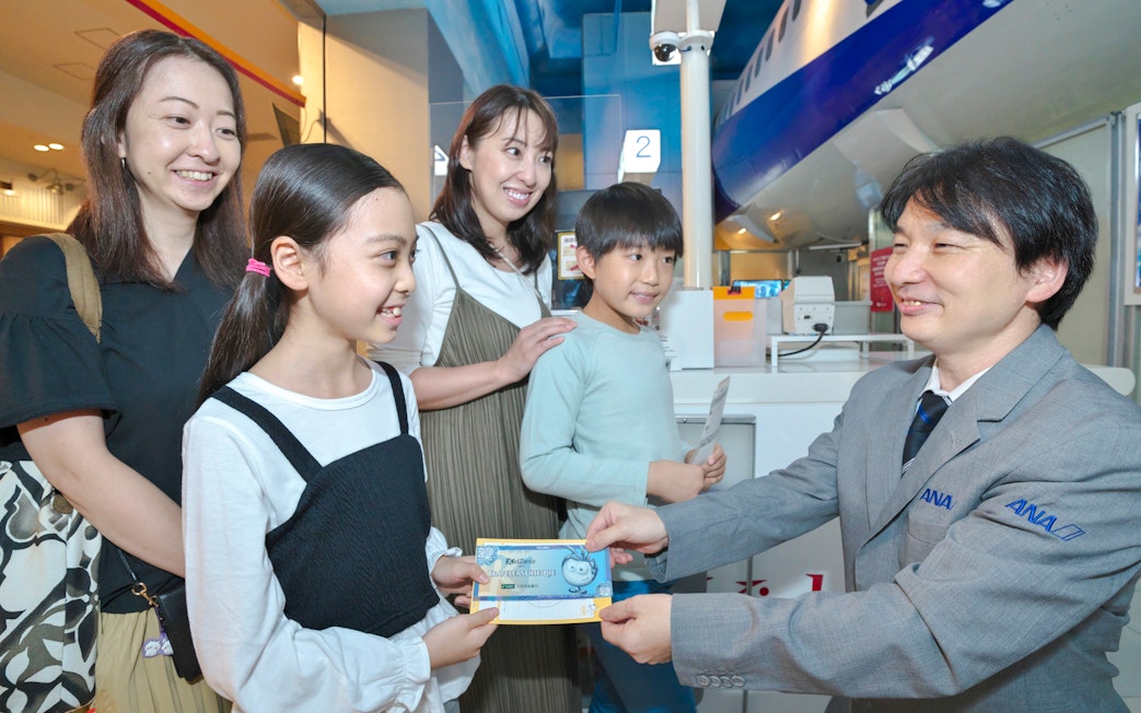 Child receiving certificate at KidZania Tokyo with family and staff member.