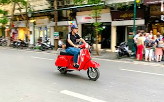 Person riding a red Vespa on a street in Hanoi during a photo tour.