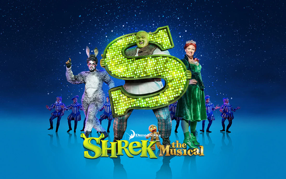 Shrek The Musical characters on stage with a large green "S" sign.