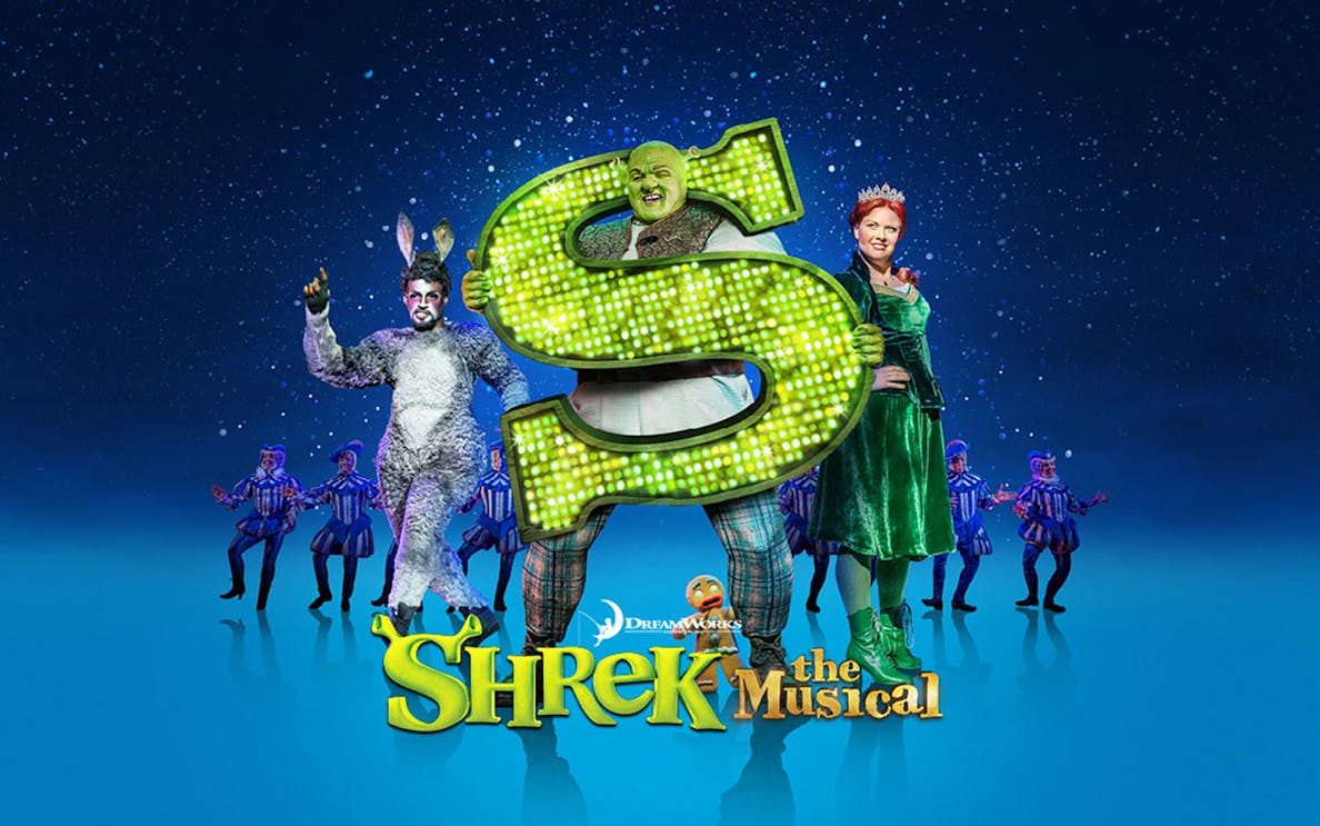 Shrek The Musical characters on stage with a large green "S" sign.
