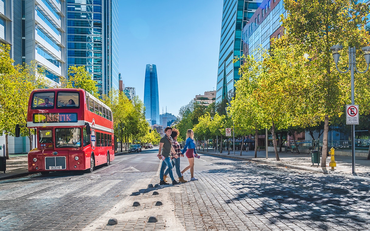 Red double-decker bus on Santiago street with modern buildings and people crossing.