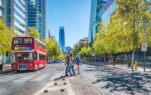 Red double-decker bus on Santiago street with modern buildings and people crossing.