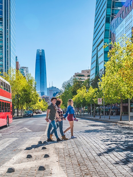 Red double-decker bus on Santiago street with modern buildings and people crossing.