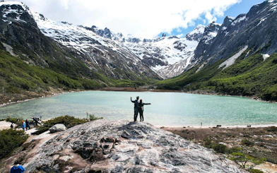 Trekking couple at Esmeralda Lake with snow-capped mountains in Ushuaia, Argentina.