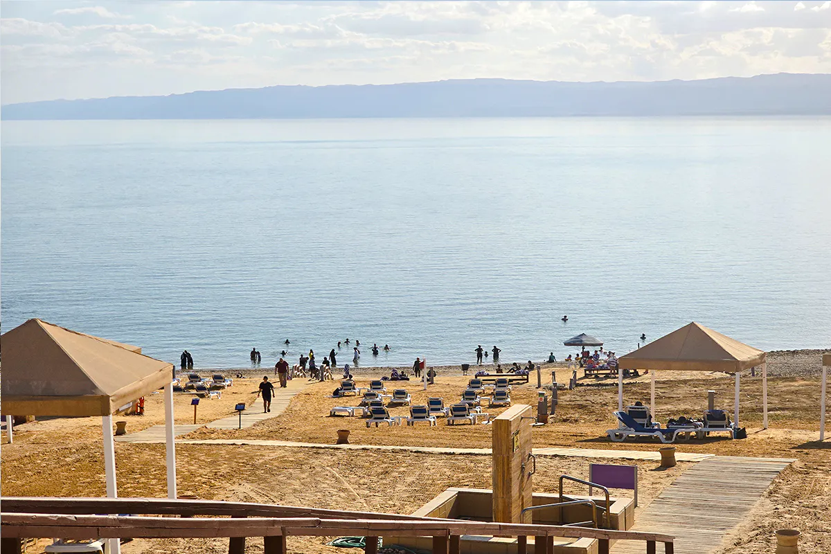 Visitors relaxing and floating in the Dead Sea near Amman, with beach chairs and canopies.