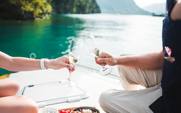 Couple toasting with prosecco on a speedboat in a scenic lake setting.