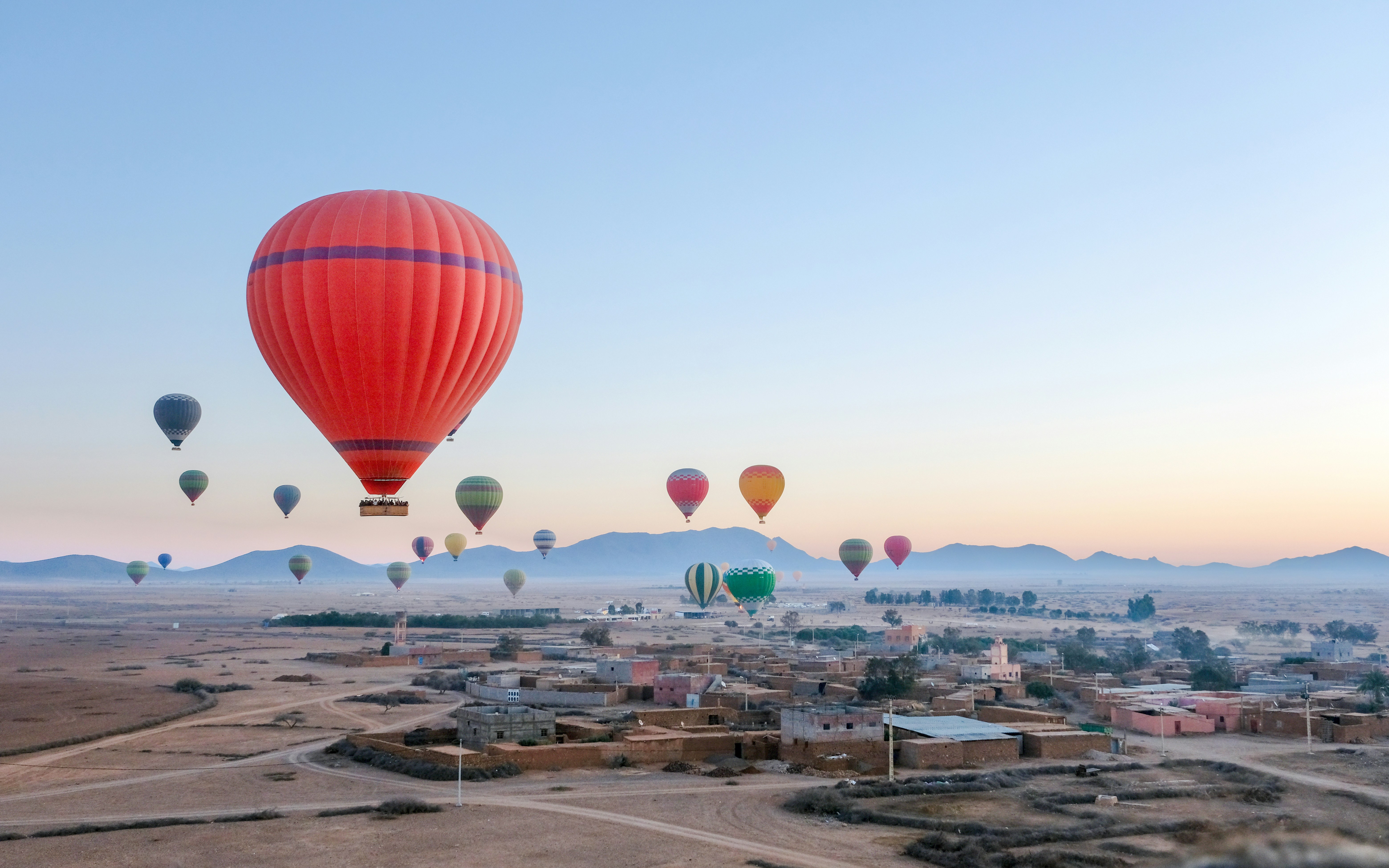 Hot air balloons floating over a Berber village near Marrakech at sunrise.