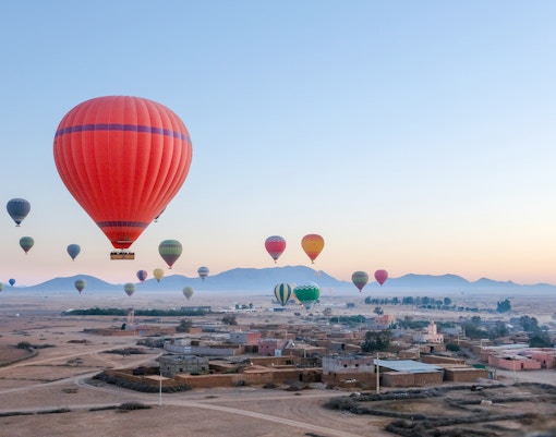 Hot air balloons floating over a Berber village near Marrakech at sunrise.