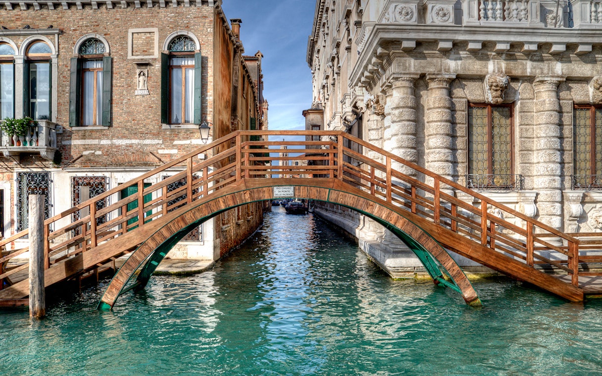 Wooden bridge over canal between historic buildings in Venice near Ca' Rezzonico.