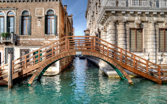 Wooden bridge over canal between historic buildings in Venice near Ca' Rezzonico.