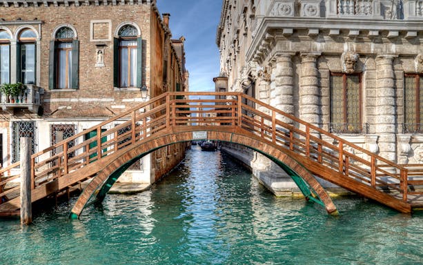 Wooden bridge over canal between historic buildings in Venice near Ca' Rezzonico.