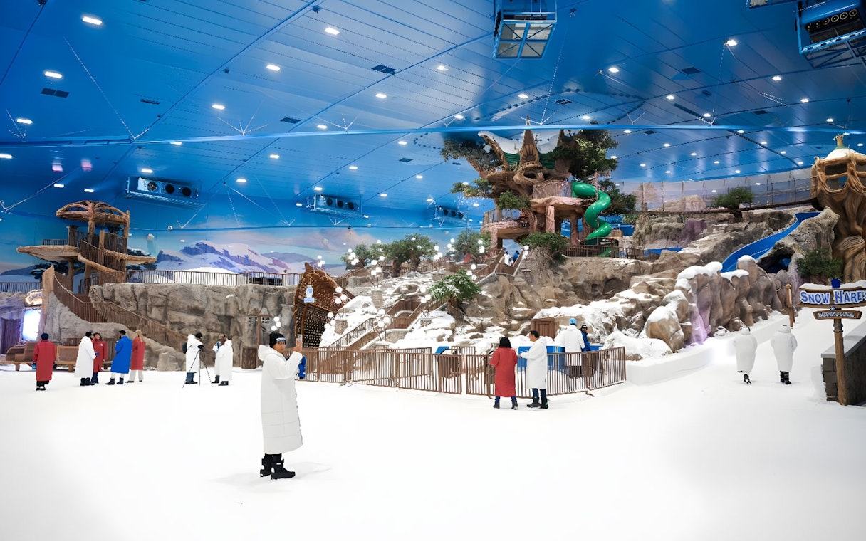 Visitors exploring Snow Abu Dhabi's indoor snow park with slides and snowy landscapes.