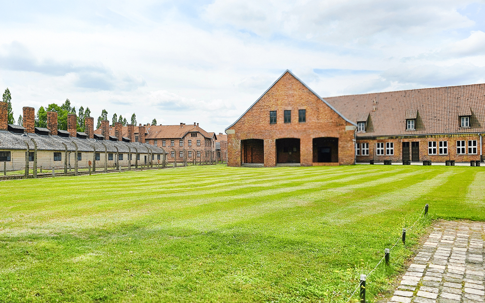 Auschwitz Birkenau barracks and main building with green lawn in foreground.