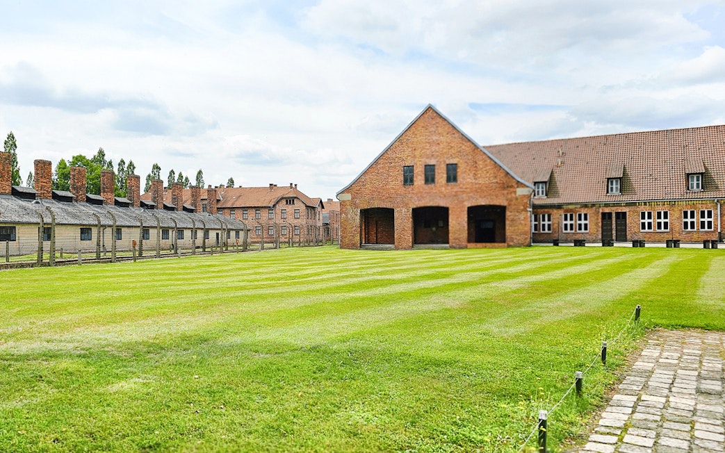 Auschwitz Birkenau barracks and main building with green lawn in foreground.