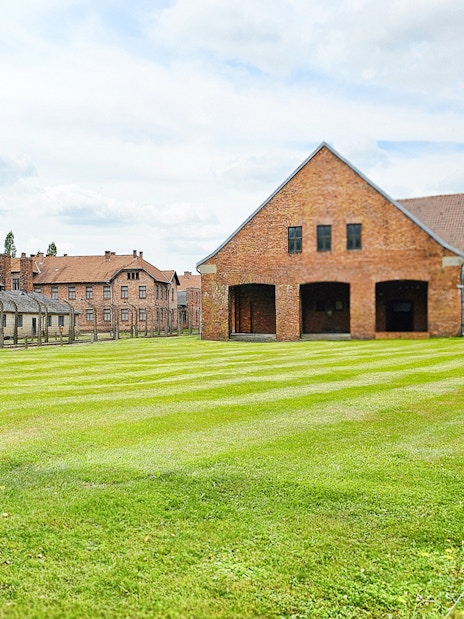 Auschwitz Birkenau barracks and main building with green lawn in foreground.